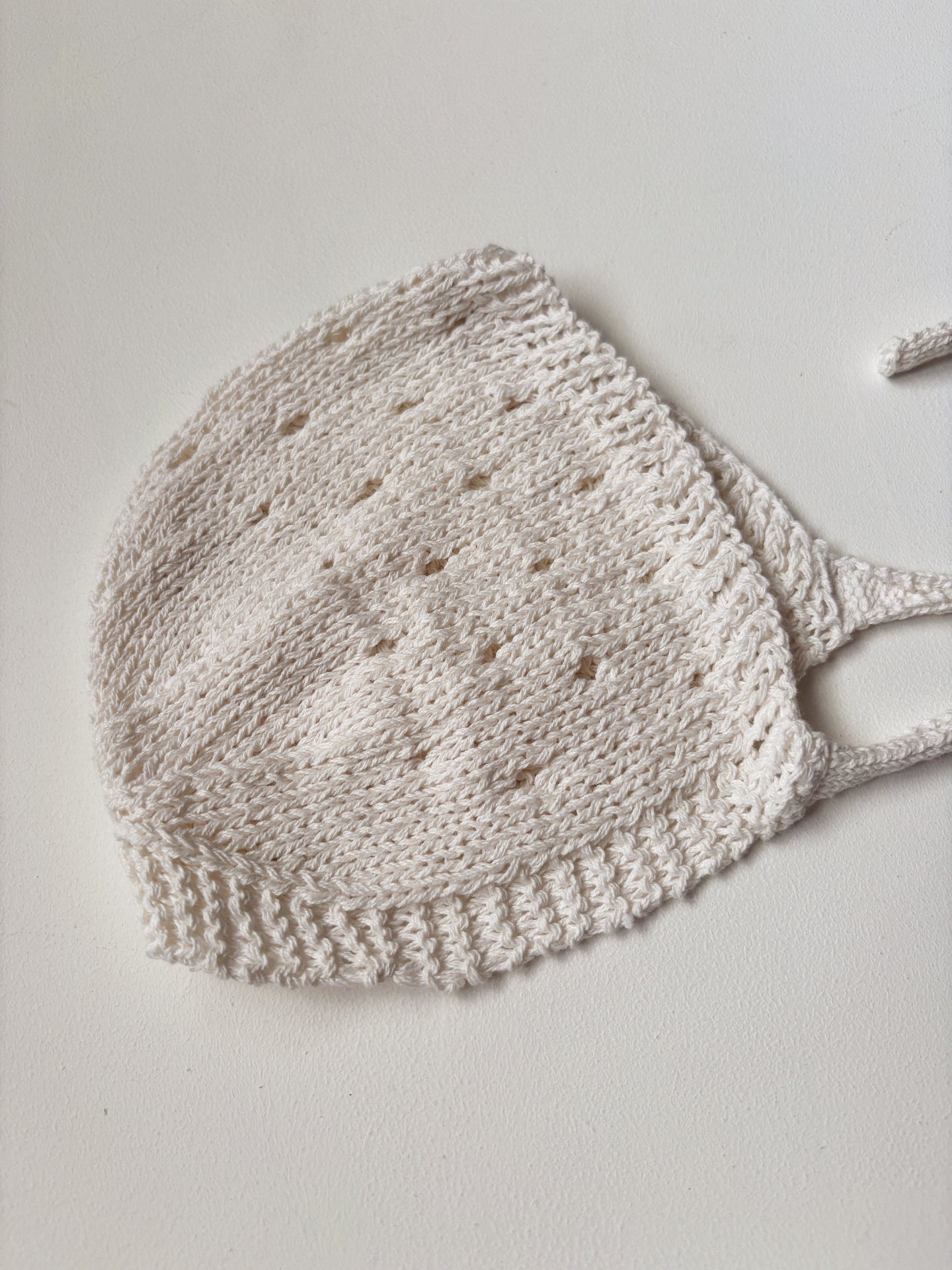 image shows a cream knitted baby bonnet