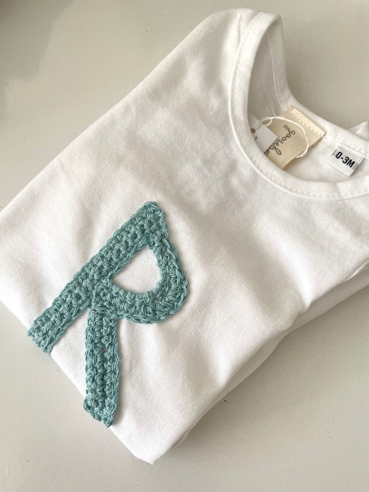 Image shows an organic cotton baby vest personalised with a crochet initial
