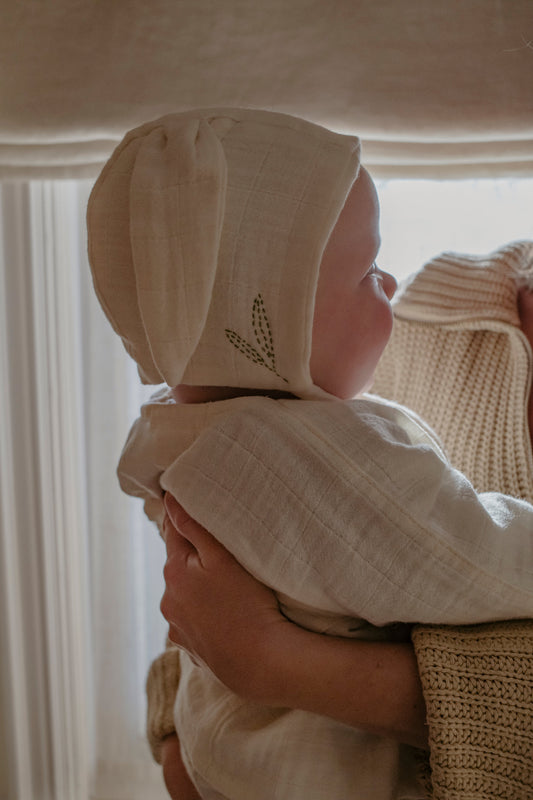 Baby wearing an organic cotton bunny bonnet being held, with a blurred background