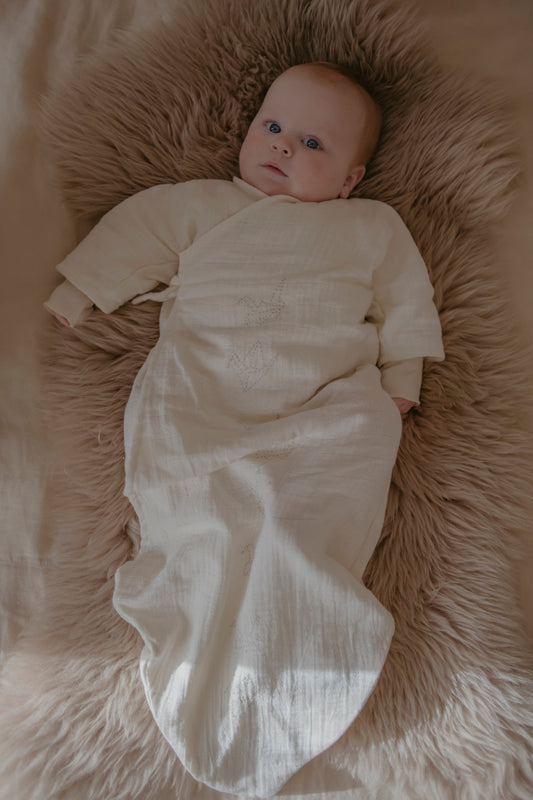 Baby wrapped in a muslin nightgown lying on a fluffy brown rug