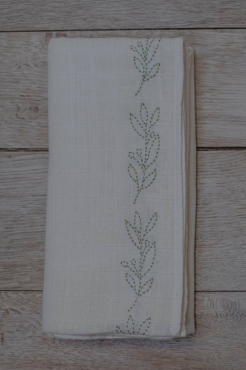organic cotton muslin swaddle with green embroidery on a wooden surface