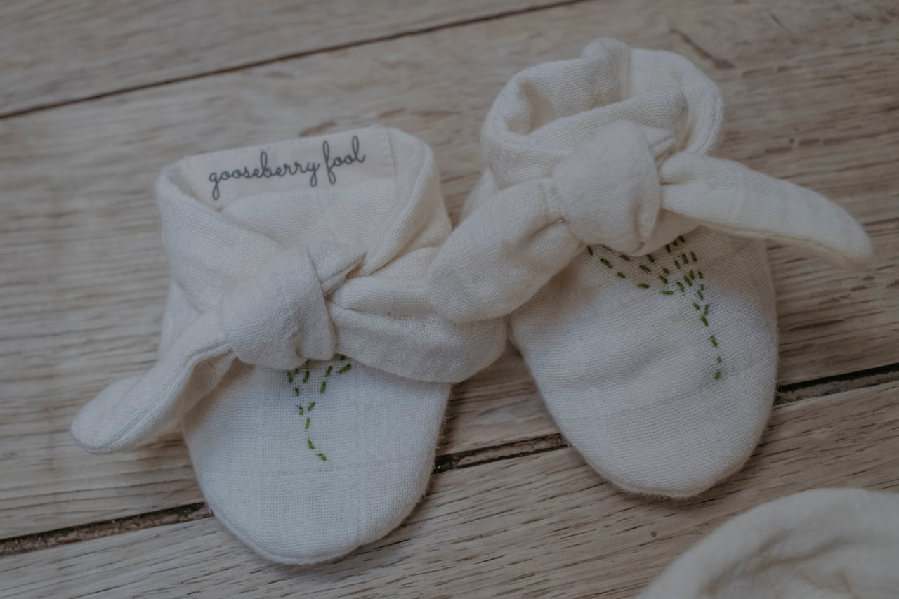 Pair of white baby booties with a tie and hand embroidery details