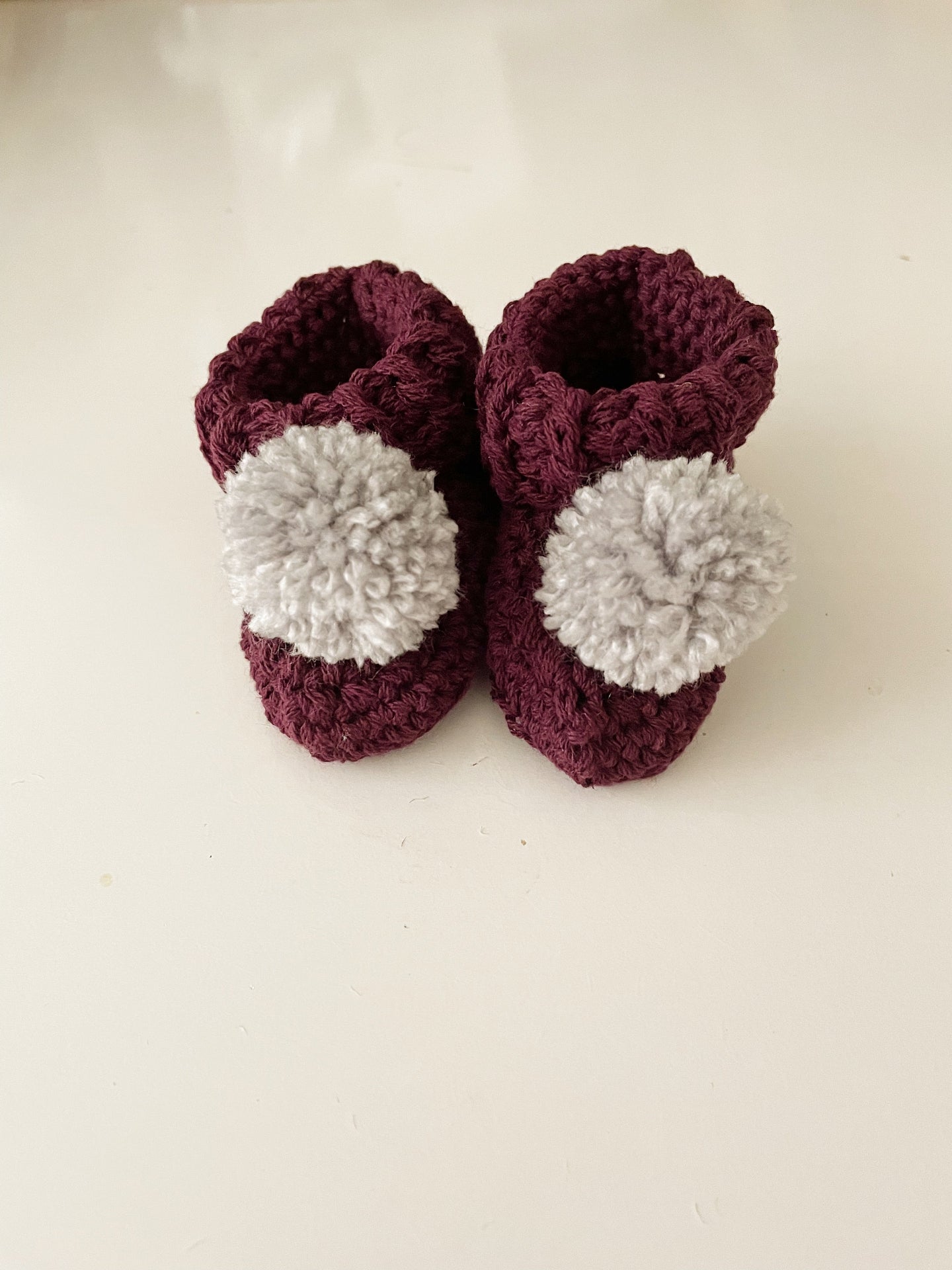 Image shows a pair of mulberry coloured organic cotton baby booties with light grey pom pom