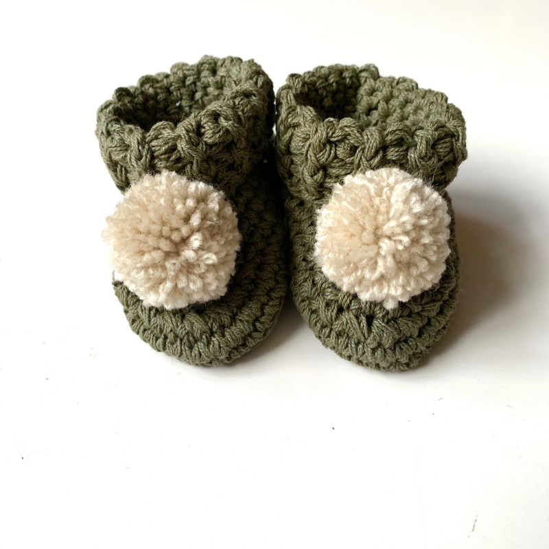 image shows a pair of olive coloured organic cotton baby booties with an oatmeal pom pom